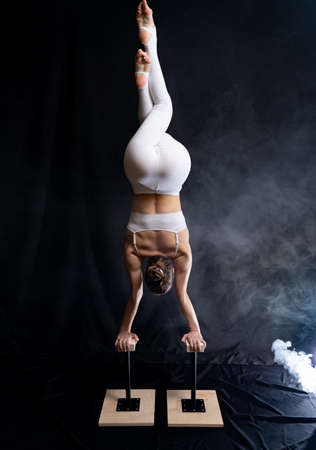 Flexible circus artist - female acrobat doing handstand on the back and smoker backgroundの写真素材