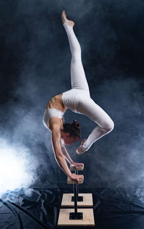 Flexible circus artist - female acrobat doing handstand on the back and smoker backgroundの写真素材