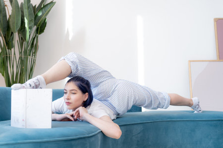 Flexible young girl in pajamas reading book in a creative way indoor. Yoga, self-discovery and self-knowledge conceptの写真素材