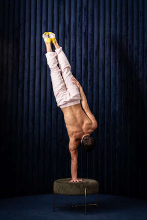 Muscular man doing handstand by one hand at home. Concept of yoga, creativity and healthy lifestyleの写真素材