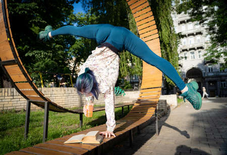 Young flexible woman read book on the bench and keep on one hand. Possibility, passion and goal...