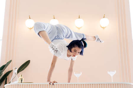 Flexible woman stands by the hands on the table with glasses of water. Concept of yoga and healthy lifestyleの写真素材