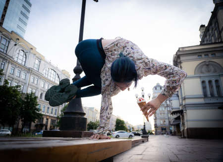 Flexible young woman eat ice cream and keep balance on one hand. Concept of yoga, healthy lifestyle and handstandの写真素材