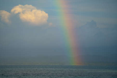 Rainbow over cloudy sky with sea and mountain landの写真素材