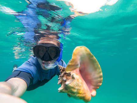 Caucasian man holding and huge conch shell during snorkeling underwater. Travel, vacation l and...