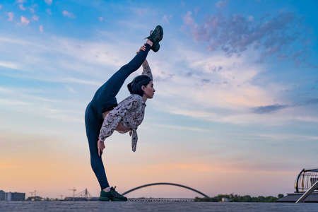 Silhouette of flexible yoga woman keeping balance in split on dramatic sunset and cityscape. Concept of healthy lifestyle and healthcareの写真素材