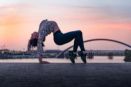 Silhouette of flexible yoga woman bending her back on dramatic sunset and cityscape. Concept of healthy lifestyle and healthcareの写真素材