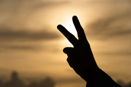 Happy people enjoying nature. Peace two fingers hand sign in front of a sunset.の写真素材