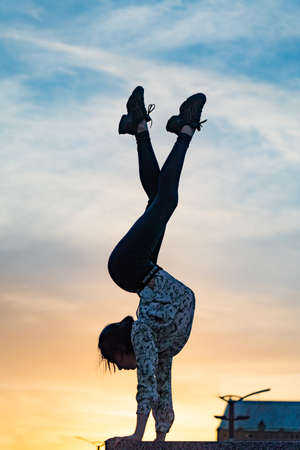 Silhouette of flexible woman gymnast doing handstand on the dramatic sunset. Concept of willpower, motivation and passionの写真素材