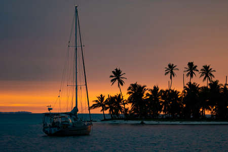 Beautiful sunset with silhouette of sailboat and palm trees on island. Vacation and adventure conceptの写真素材