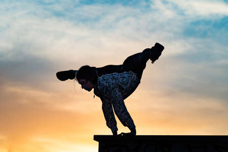 Silhouette of flexible female circus artist doing handstand on the dramatic sunset. Concept of individuality, creativity and outstandingの写真素材
