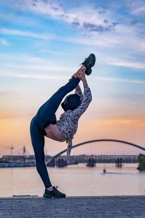 Silhouette of flexible female woman keeps balance gymnastic on split on the dramatic sunset. Concept of individuality, creativity and outstandingの写真素材