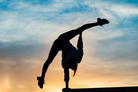 Silhouette of female flexible acrobat doing handstand on the dramatic sunset. Concept of individuality, creativity and outstandingの写真素材