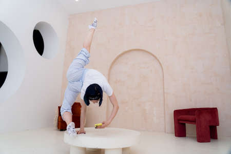 Flexible girl keep balance on one hand while smartphone at home. Concept of boredom during COVID self isolationの写真素材