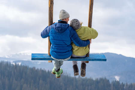 A loving couple on a swing in the winter mountains. Relationship, vacation, travel concept