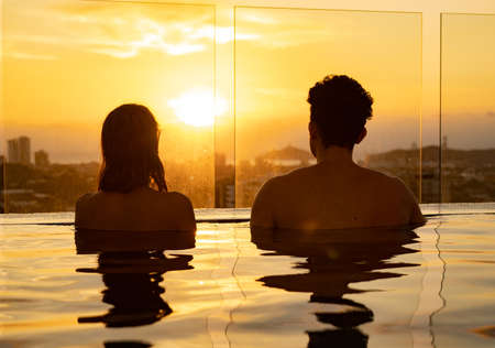 Silhouette of Loving couple in the infinity pole water during sunset. Romantic vacation conceptの写真素材