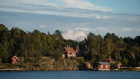 Beautiful Red Swedish Wooden Log Cabin Houses On Rocky Island Coast In Summer with forestの写真素材