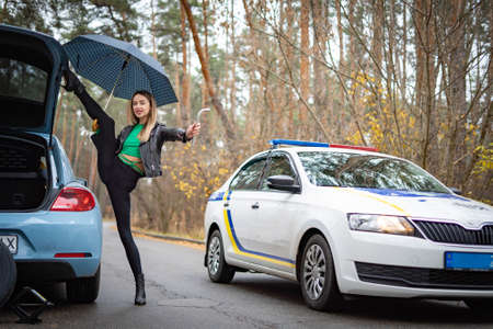 Sexy woman on the hills stopping the police car on the road. Concept of seduction and crimeの写真素材