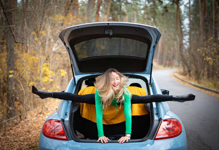 Sexy, flexible woman in the car on the road doing stretching . Concept of individuality, creativity and outstandingの写真素材