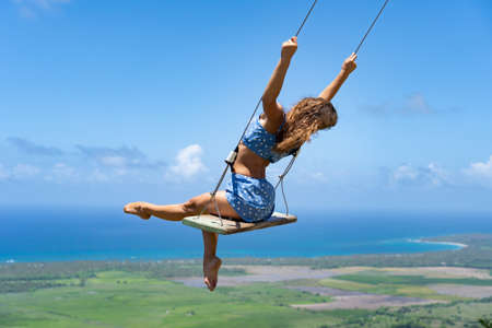 Young beautiful caucasian woman on the rope swing with sea and sky background. Concept of dream and happinessの写真素材