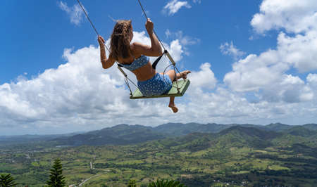 Young woman on the rope swing with sky and mountains background. Concept of freedom and happiness