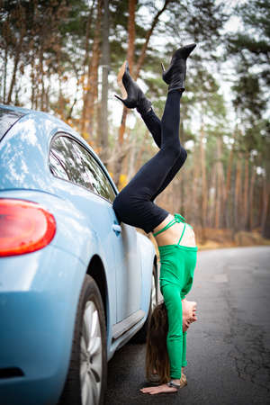 Sexy, flexible woman on the heels with car on the road. Concept of sexuality and seductionの写真素材