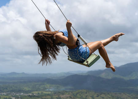 Young woman on the rope swing with sky and mountains background. Concept of vacation and leisureの写真素材