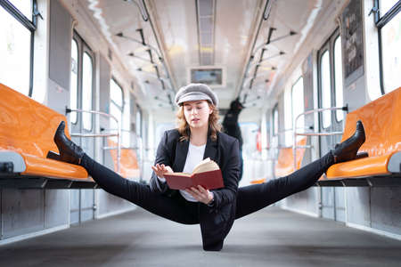 Very flexible woman wearing mask reading book in the subway car sitting in the gymnastic split. Concept of healthy lifestyle and educationの写真素材