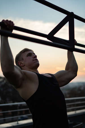 Muscular man doing pullups on sunset sky background. Calisthenics, healthy lifestyle and workout conceptの写真素材