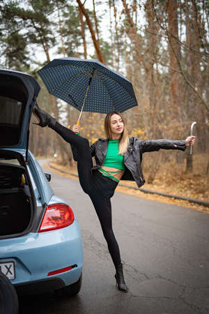 Sexy, flexible woman in the car on the road doing stretching . Concept of individuality, creativity and self-confidenceの写真素材
