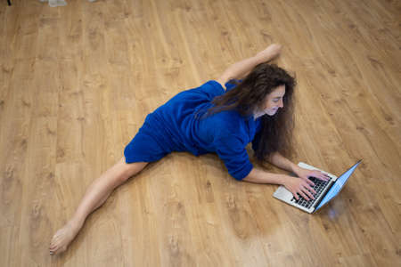 flexible woman exercising at home in front of her laptop, stretching her legs in the split. Concept of yoga and healthy lifestyleの写真素材