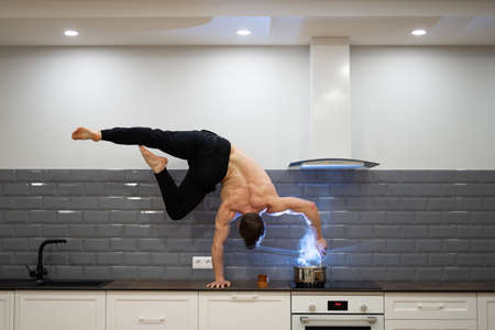 Man keeps balance on one hand and cooks food in the kitchen. Healthy lifestyle, yoga and wellness concept.の写真素材