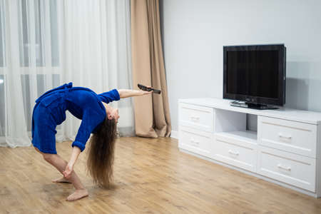 flexible woman exercising at home in front of tv screen, stretching her back. Concept of individuality, creativity and self-confidence.の写真素材