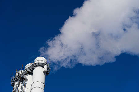 Air pollution by smoke coming out of pipes against blue sky. Concept of pollution, environmental problems and emissionsの写真素材