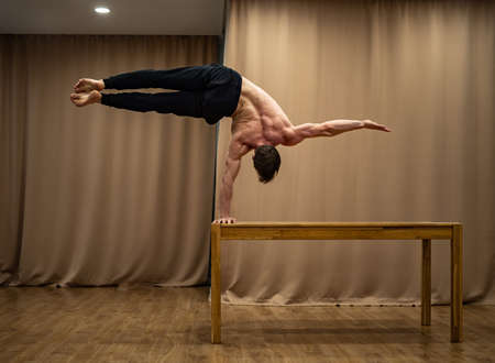 A muscular man keeps balance on one hand indoor. Concept of healthy lifestyle, yoga and handstandの写真素材