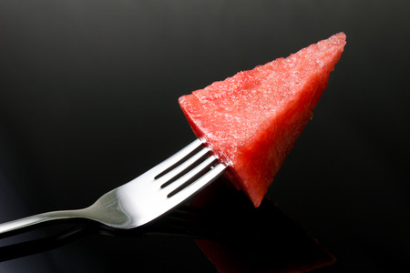 Slice of water-melon with fork on black background.