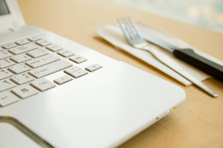 White laptop with fork and knife on wood table background.