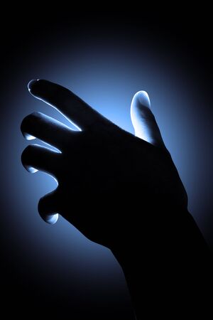 Abstract silhouette hand reaching with blue light background.の写真素材