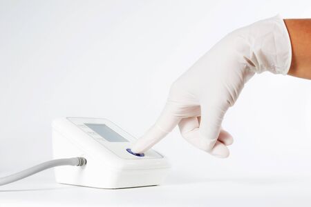 Female hands wear glove press start button on blood-pressure meter isolated on white background.の写真素材