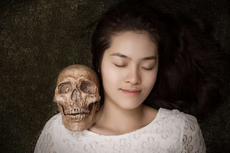 Young Asian woman close her eyes and lying on the ground with skull on her shoulder.