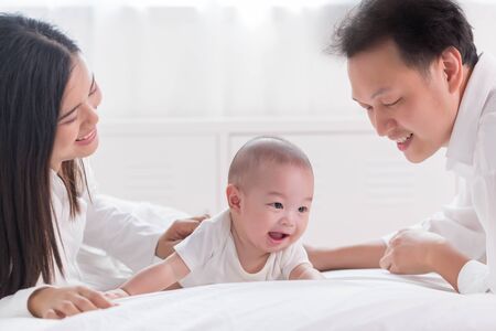Young happy Asian mom dad and newborn baby playing at sweet home.