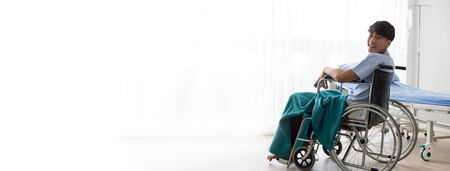 Young Asian man sitting on a wheelchair in the hospital with smiley face.