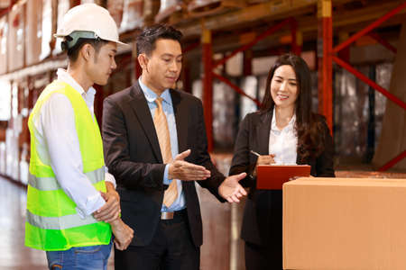 Asian Warehouse manager and male worker as engineer interacting talking checking inventory, manager team working at the storehouse.の写真素材