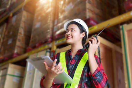 Warehouse logistic management business; young Asian woman wearing reflective safty vest and white...