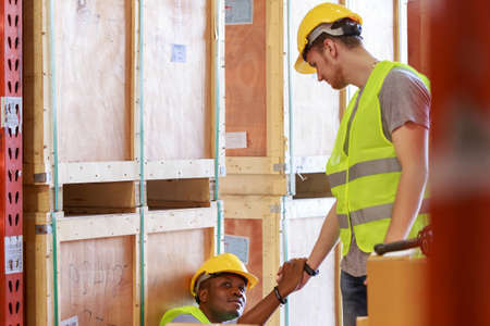Young Caucasian warehouse industrial worker helping African man  getting up from accident....