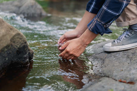 Close up young adult human hand touching stream water in the forest while he hiking, peaceful serenity moment with nature.の写真素材