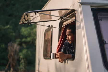 Handsome young Asian man, traveler on road trip, sit inside camping van in the morning. Cosy...