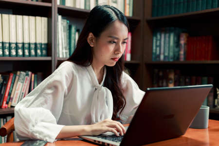 Candid of young attractive Asian woman working on laptop computer late at night.