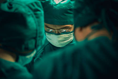 Asian Medical Team Performing Surgical Operation in Modern Operating Room. Doctors and Nurse in green uniform concentrate working in the hospital.の写真素材