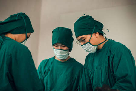 Asian Medical Team Performing Surgical Operation in Modern Operating Room. Doctors and Nurse in green uniform concentrate working in the hospital.の写真素材